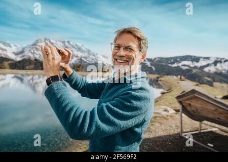 Homme mûr souriant prenant une photo de la vue à Hochkonig, Salzburger Land, Autriche Banque D'Images