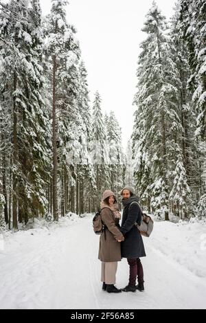 Couple avec sac à dos tenant les mains tout en se tenant dans la forêt pendant hiver Banque D'Images