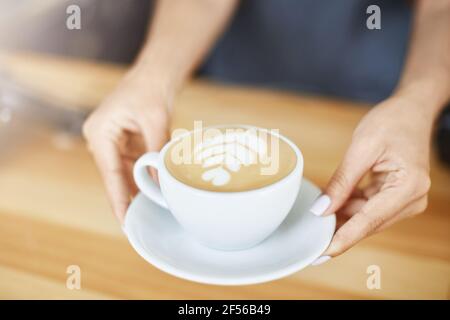 Gros plan des mains de femme servant un cappuccino dans une tasse avec latte art. Concept Barista. Banque D'Images