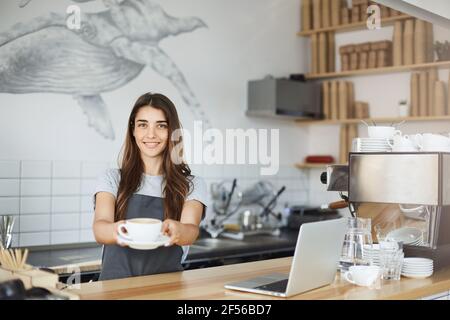 Le jeune barista sert le meilleur cappuccino au monde. Banque D'Images