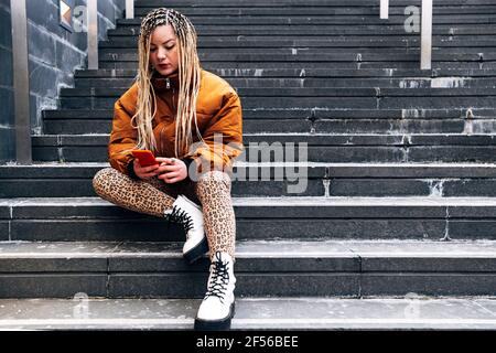 Jeune femme portant une veste sur un téléphone portable lorsqu'elle est assise étapes Banque D'Images