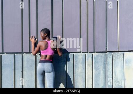 Jeune femme souriante s'exerçant tout en s'appuyant sur le mur Banque D'Images