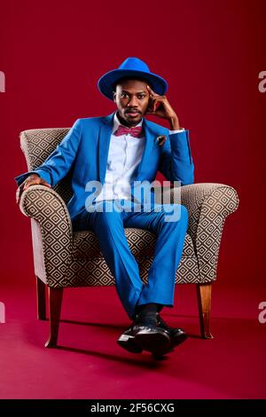 Homme adulte moyen avec tête dans la main assis sur une chaise sur fond rouge Banque D'Images