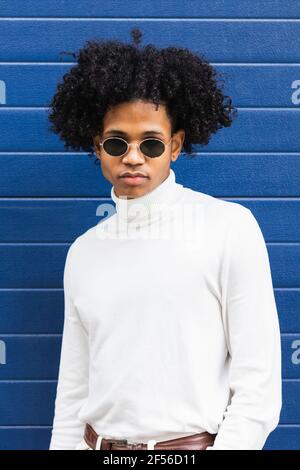 Adolescent portant des lunettes de soleil en regardant contre le mur bleu Banque D'Images