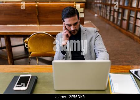 Homme d'affaires travaillant sur un ordinateur portable tout en étant assis dans la bibliothèque Banque D'Images