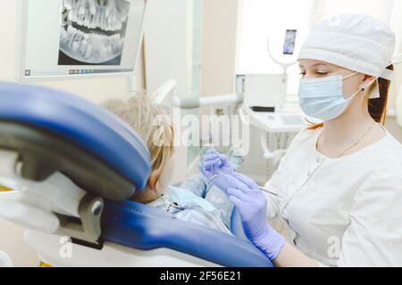 Femme dentiste portant un masque facial de protection traitant la petite fille à clinique Banque D'Images