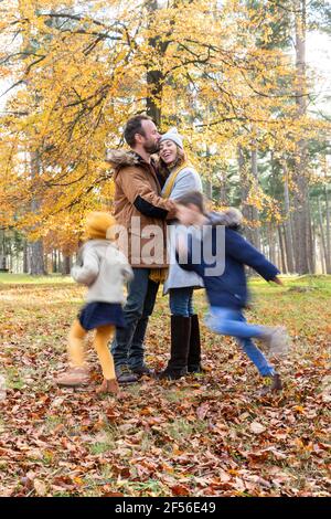 Homme embrassant la femme en se tenant debout avec des enfants jouant autour dans forêt Banque D'Images