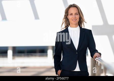 Femme d'affaires souriante avec les mains dans les poches debout sur la terrasse du bâtiment Banque D'Images