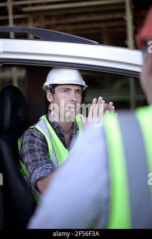 Deux ouvriers du bâtiment bavardent en voiture Banque D'Images