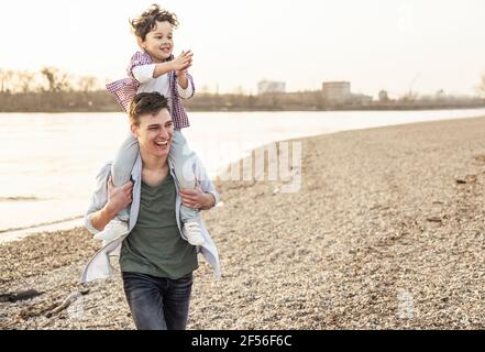 Joyeux jeune homme marchant tout en portant un garçon sur les épaules lac Banque D'Images