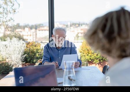 Femme assise sur un ordinateur portable avec un homme en arrière-plan travaillant à accueil Banque D'Images