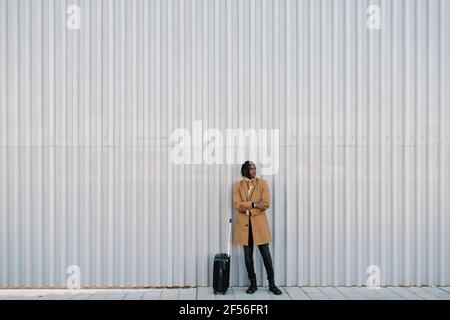 Homme avec une valise debout contre un mur gris tout en regardant loin Banque D'Images