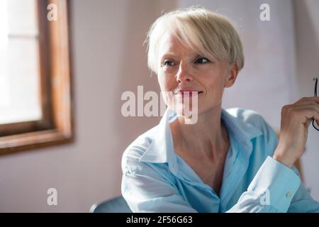 Femme entrepreneur souriante qui regarde loin tout en étant assise à la maison Banque D'Images