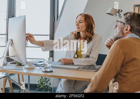 Femme médecin expliquant par ordinateur tout en étant assise avec le patient à cabinet du médecin Banque D'Images