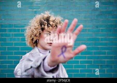 Femme aux cheveux bouclés montrant le symbole du ruban du cancer du côlon à portée de main Banque D'Images