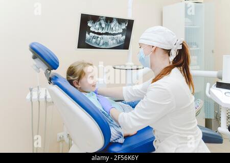 Une femme dentiste pose un drapé dentaire sur une petite fille assise chaise de dentistes Banque D'Images