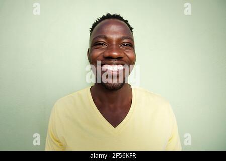 Portrait grand angle de drôle de jeune africain souriant contre mur vert Banque D'Images