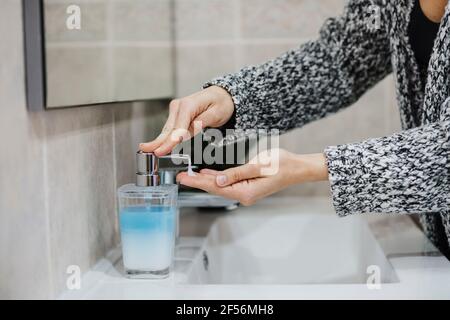Femme vaporisant du savon liquide à la main à l'évier dans la salle de bains Banque D'Images