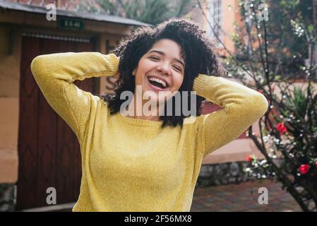 Femme gaie en chandail jaune jouant avec les cheveux à l'arrière cour Banque D'Images