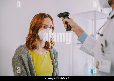 Médecin vérifiant la température du patient à l'aide d'un thermomètre infrarouge tout en étant debout salle d'examen Banque D'Images