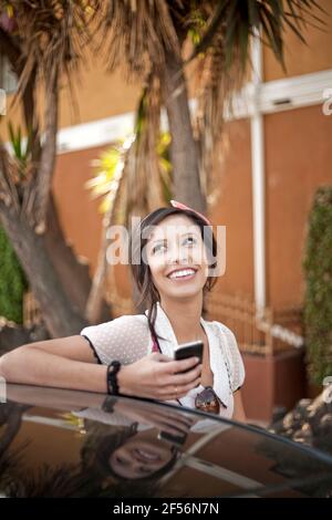Femme souriante avec téléphone portable, à l'écart, debout voiture Banque D'Images