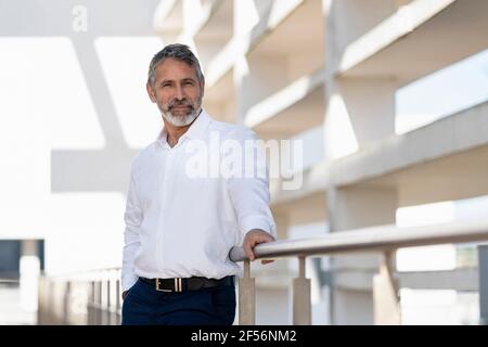 Homme professionnel souriant debout près des balustrades sur la terrasse du bureau Banque D'Images