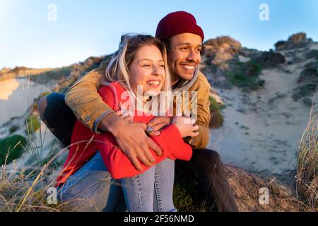 Homme portant un chapeau en tricot embrassant la belle femme tout en étant assis sur dune de sable Banque D'Images