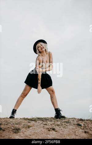 Jeune femme portant un chapeau debout sur une jambe contre le ciel Banque D'Images