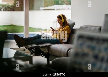 Femme d'âge mûr écoutant de la musique tout en étant assise sur un fauteuil inclinable séjour Banque D'Images