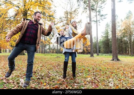 Une fille souriante se balançant tout en tenant les mains de parents debout forêt Banque D'Images