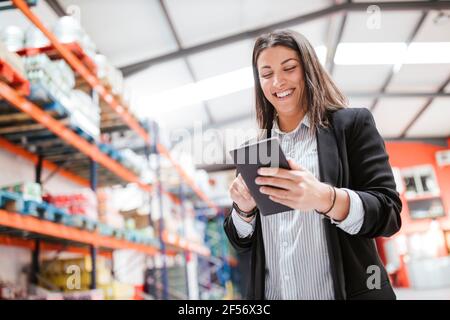 Une femme souriante qui utilise une tablette numérique dans un entrepôt de distribution éclairé Banque D'Images