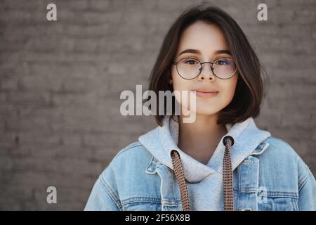 Portrait en gros plan insouciante optimiste jeune étudiante à cheveux courts en lunettes regardant avec impatience les occasions de la vie, souriant regard rêveur Banque D'Images