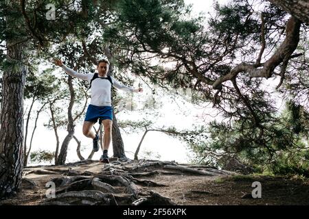 Coureur de fond sautant sur les racines tout en courant dans la forêt Banque D'Images