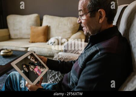 Homme senior souriant en appel vidéo avec ses petits-enfants Tablette numérique à la maison pendant COVID-19 Banque D'Images