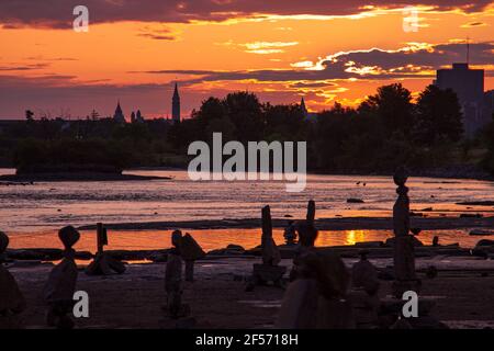 Silhouette de l'horizon d'Ottawa et de la colline du Parlement au lever du soleil sur la rivière aux couleurs vives. Des sculptures en pierre se trouvent sur la plage au premier plan. Banque D'Images