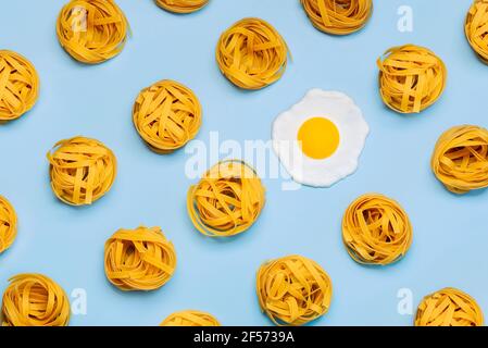 Vue de dessus du motif créatif fait de nids de tagliatelle crus pâtes et un œuf frit sur fond bleu Banque D'Images