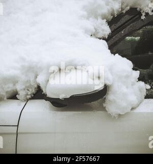 Fragment de voiture blanche recouverte de neige avec un rétroviseur replié et des gouttes sur le verre Banque D'Images