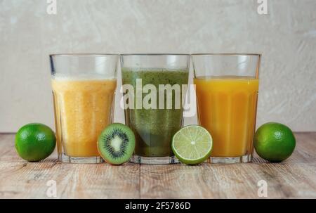 Trois grands verres avec des smoothies aux kiwis et aux épinards dans une rangée entourée de fruits sur une table en bois. Le concept de perte de poids et de nutrition appropriée. Banque D'Images