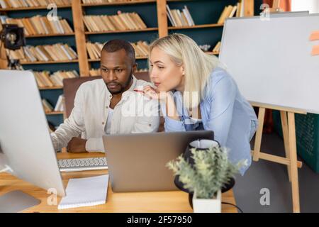 Des collègues multiethniques sérieux utilisant l'ordinateur, recherchant des idées de projet. Les jeunes employés adultes travaillent ensemble dans un bureau moderne, développant de nouveaux Banque D'Images