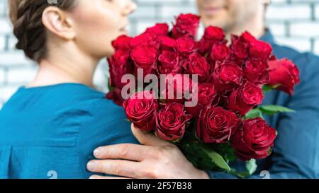 Un homme en costume embrasse une jolie petite amie et lui donne un luxueux bouquet de roses rouges. Un cadeau romantique pour la Saint-Valentin, l'anniversaire de mariage. Banque D'Images