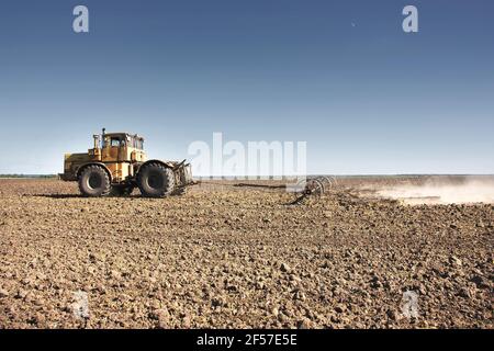 Grand tracteur jaune équipé d'une herse travaillant sur le terrain. Banque D'Images