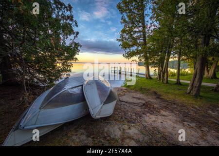 Barques sur Sunset Lake. Groupe de barques d'aluminium sur la plage d'un lac au lever du soleil avec un quai en bois. Parc national d'Indian Lake, Manistique, Michigan. Banque D'Images