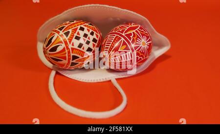 Concept du coronavirus de quarantaine de Pâques. Joyeuses Pâques, préparation pour les vacances. Oeufs de pâques décorés en couleur en nid avec masque protecteur sur bac rouge Banque D'Images