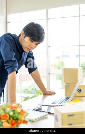 Jeune homme lance une petite entreprise (PME) en livrant des produits emballés dans des boîtes par le biais d'un système logistique depuis le bureau à domicile, la livraison de colis, en ligne m Banque D'Images