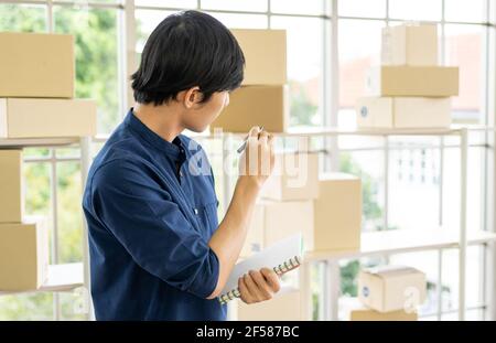 Jeune homme lance une petite entreprise (PME) en livrant des produits emballés dans des boîtes par le biais d'un système logistique depuis le bureau à domicile, la livraison de colis, en ligne m Banque D'Images