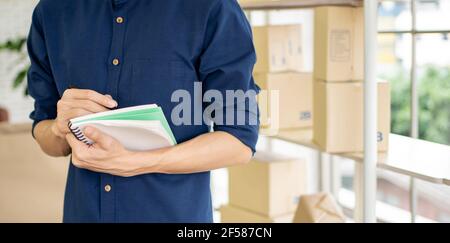Jeune homme lance une petite entreprise (PME) en livrant des produits emballés dans des boîtes par le biais d'un système logistique depuis le bureau à domicile, la livraison de colis, en ligne m Banque D'Images