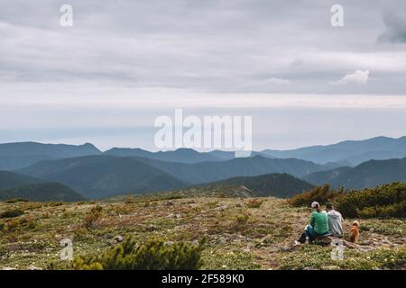 Un couple marié avec un chien est assis au sommet de la colline et admirent le magnifique paysage de montagne. Ils se reposent après l'ascension. Visite le week-end. Banque D'Images