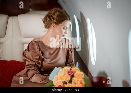 une jolie femme blonde habillée dans une élégante robe beige est présente dans un siège confortable sur un jet privé Banque D'Images