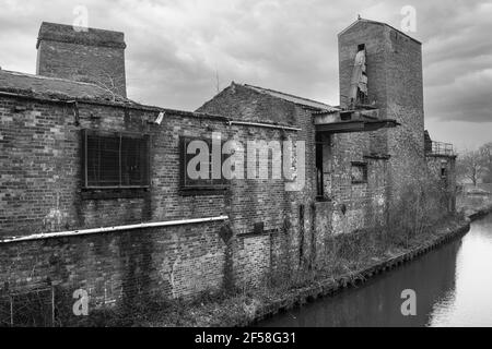 Photographie en noir et blanc montrant la désintégration urbaine. Un vieux bâtiment négligé abandonné par le côté d'un canal Banque D'Images