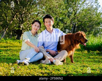 Jeune couple et chien dans le parc, assis sur le herbe Banque D'Images